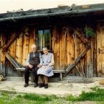 elderly couple sitting on a bench in front of a cabin